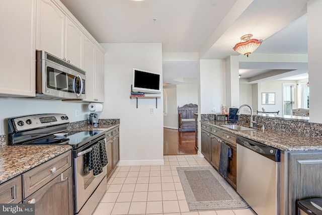 kitchen featuring a sink, dark stone countertops, stainless steel appliances, light tile patterned flooring, and white cabinets