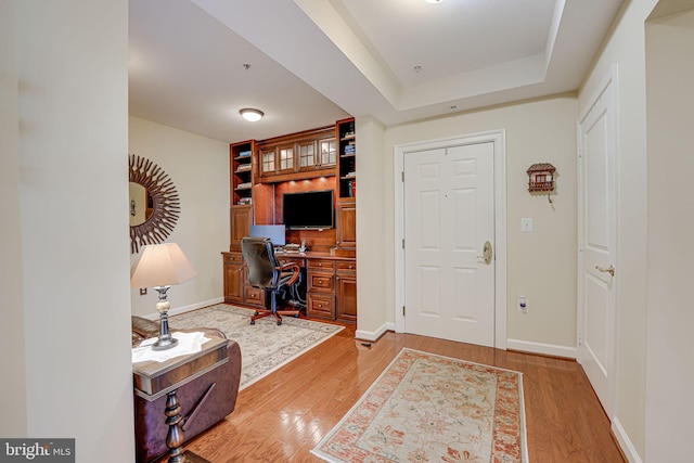 office space with a raised ceiling, light wood-style flooring, and baseboards