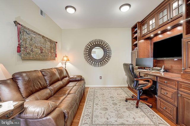 office space with visible vents, baseboards, light wood-style floors, and built in study area