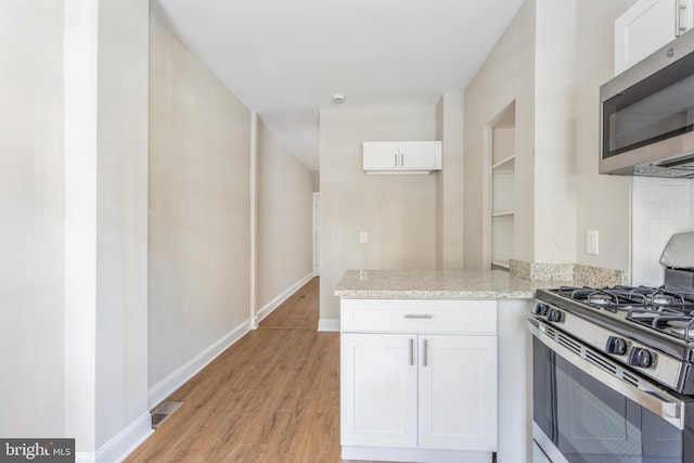 kitchen with white cabinetry, appliances with stainless steel finishes, light hardwood / wood-style floors, and light stone counters