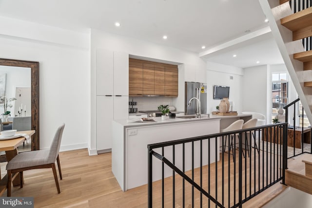 kitchen with decorative backsplash, an island with sink, white cabinets, light hardwood / wood-style flooring, and sink