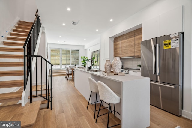 kitchen with light wood-type flooring, an island with sink, white cabinetry, a kitchen bar, and high end fridge