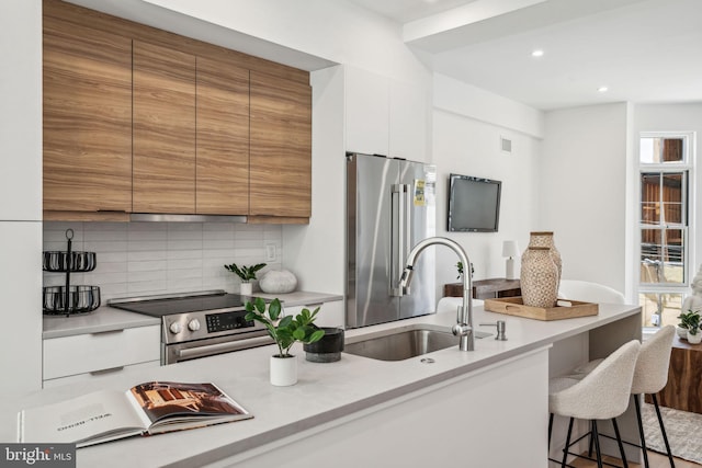 kitchen with a breakfast bar area, sink, white cabinetry, backsplash, and appliances with stainless steel finishes