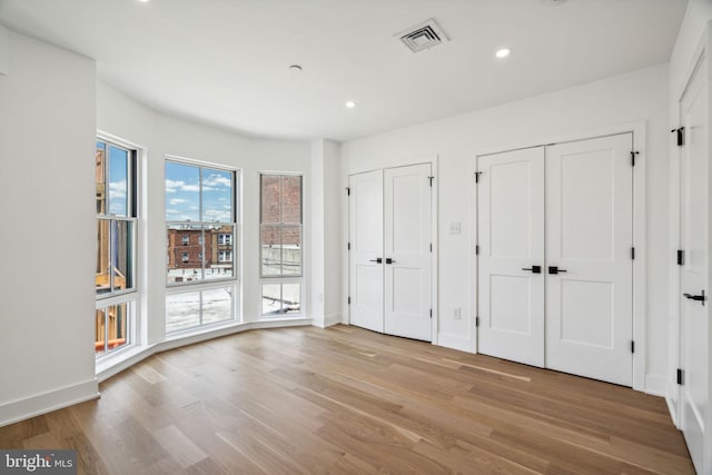 unfurnished bedroom featuring light wood-type flooring and two closets