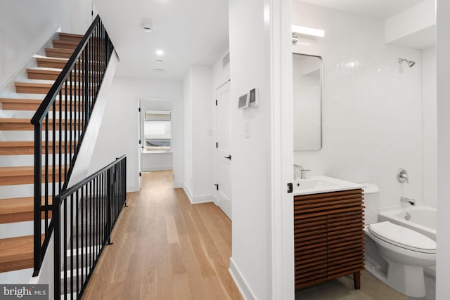 interior space featuring wood-type flooring, vanity, toilet, and tiled shower / bath