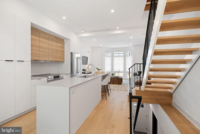 kitchen with an island with sink, white cabinets, appliances with stainless steel finishes, and light hardwood / wood-style flooring