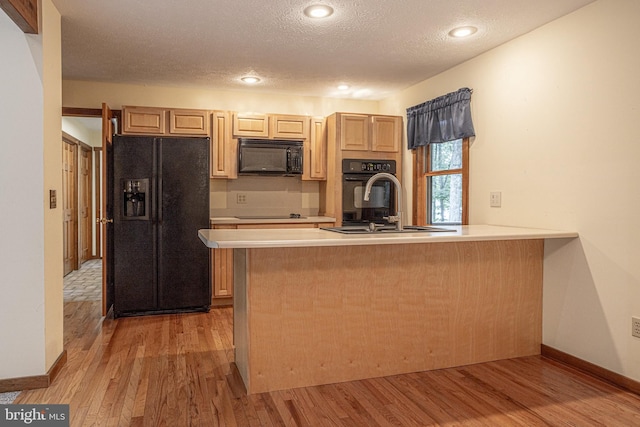 kitchen featuring a textured ceiling, black appliances, kitchen peninsula, sink, and light hardwood / wood-style floors