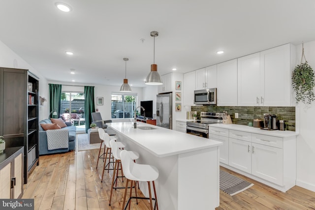 kitchen with an island with sink, stainless steel appliances, light wood-type flooring, and white cabinets