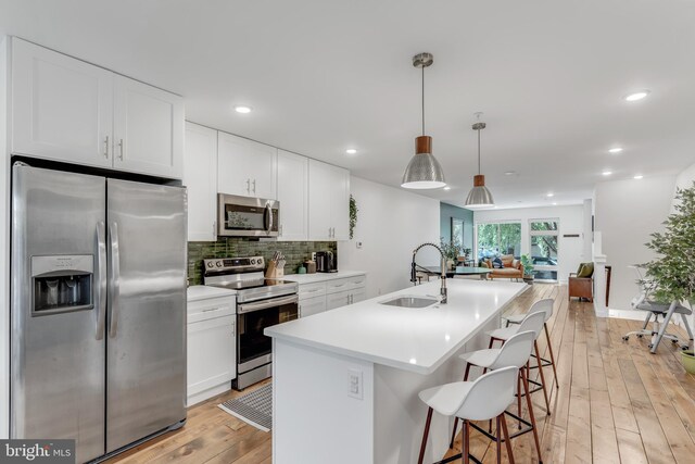 kitchen with white cabinetry, an island with sink, sink, appliances with stainless steel finishes, and light hardwood / wood-style floors