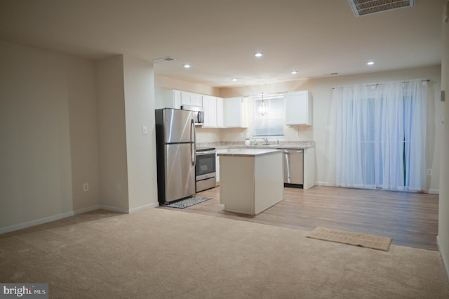 kitchen with white cabinets, appliances with stainless steel finishes, light wood-type flooring, sink, and a center island