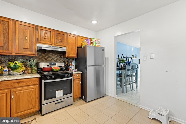 5120 Crittenden St, Hyattsville, MD 20781 - kitchen with appliances with stainless steel finishes, under cabinet range hood, brown cabinetry, backsplash, and light tile patterned floors