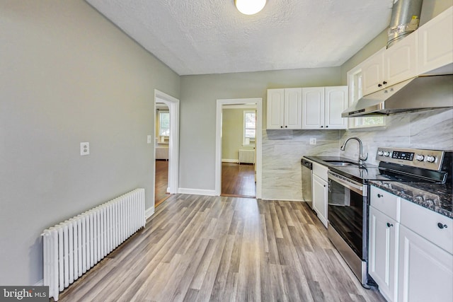 kitchen with radiator, white cabinets, sink, light hardwood / wood-style flooring, and stainless steel appliances