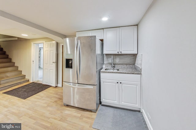 kitchen with sink, tasteful backsplash, white cabinetry, stainless steel refrigerator with ice dispenser, and light wood-type flooring