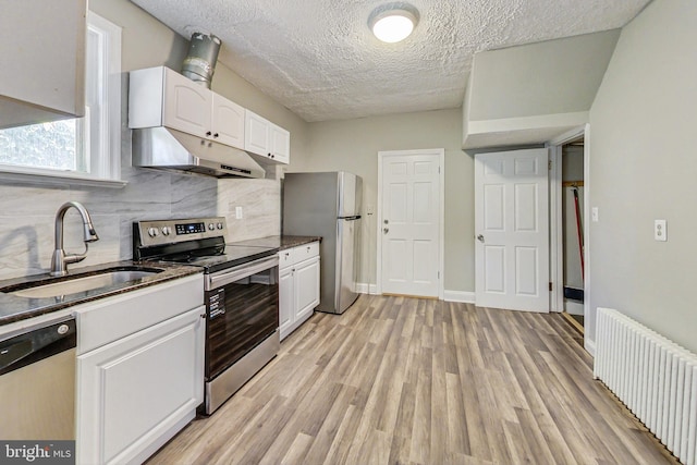 kitchen with white cabinets, stainless steel appliances, light wood-type flooring, radiator, and sink