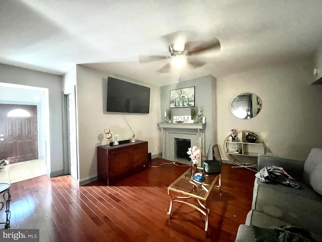 living area featuring a fireplace, baseboards, ceiling fan, and wood-type flooring