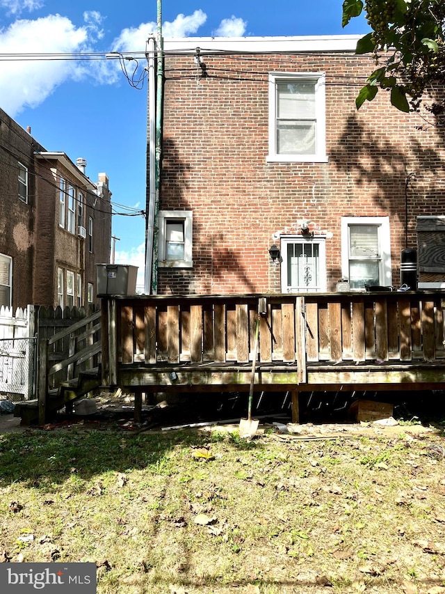 rear view of house with brick siding, a deck, and fence