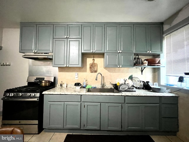 kitchen with gray cabinets, under cabinet range hood, a sink, gas stove, and light tile patterned floors