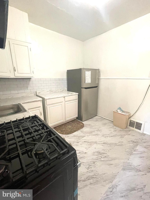 kitchen with white cabinets, stainless steel fridge, sink, black gas range oven, and decorative backsplash