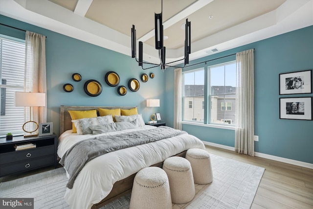 bedroom with a raised ceiling, light hardwood / wood-style flooring, multiple windows, and a notable chandelier