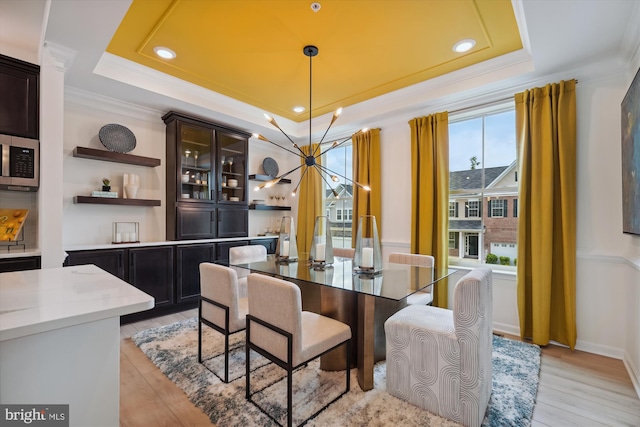 dining space with a notable chandelier, a raised ceiling, ornamental molding, and light hardwood / wood-style flooring