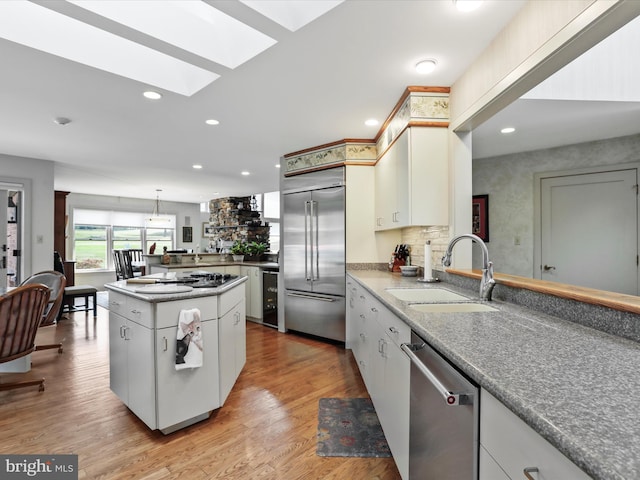 kitchen featuring appliances with stainless steel finishes, white cabinets, pendant lighting, light wood-type flooring, and sink