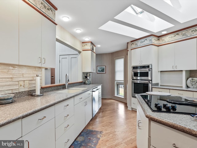 kitchen featuring appliances with stainless steel finishes, white cabinetry, light hardwood / wood-style flooring, a skylight, and sink