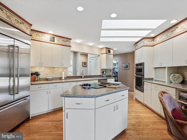 kitchen featuring a skylight, white cabinetry, stainless steel appliances, a center island, and light wood-type flooring