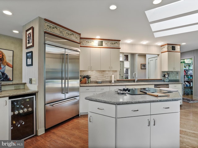 kitchen with white cabinets, wine cooler, built in refrigerator, a center island, and light hardwood / wood-style floors