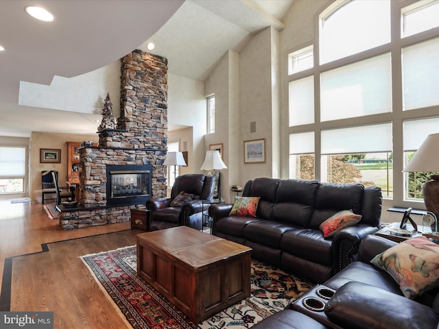 living room with high vaulted ceiling, hardwood / wood-style flooring, a healthy amount of sunlight, and a stone fireplace