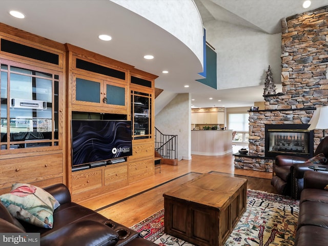 living room with wood-type flooring, a stone fireplace, and lofted ceiling