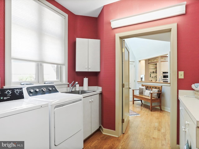 clothes washing area featuring washer and clothes dryer, cabinets, light hardwood / wood-style floors, and sink