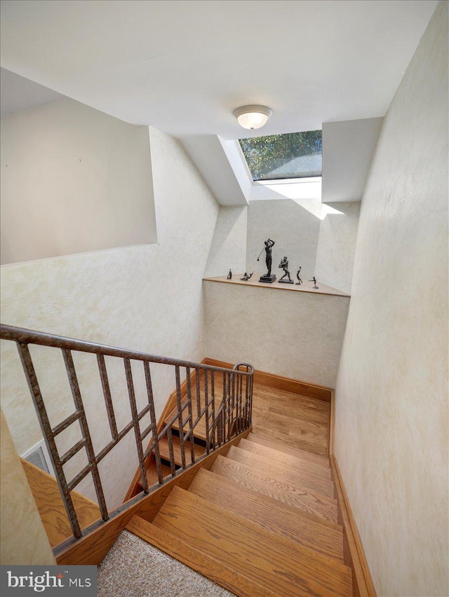 stairway with a skylight and hardwood / wood-style floors