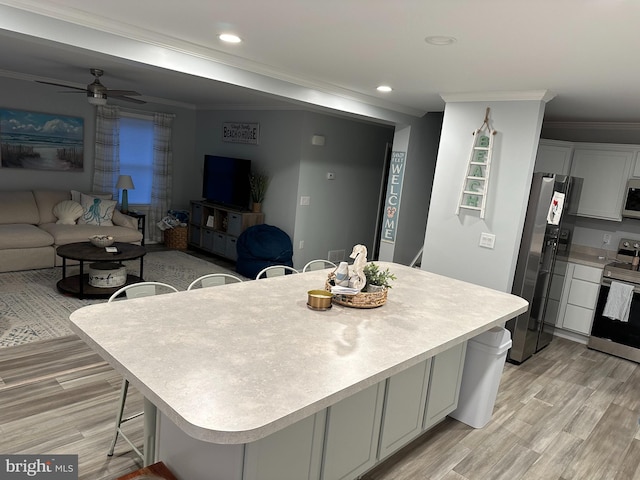 kitchen featuring light wood-type flooring, ornamental molding, a kitchen bar, ceiling fan, and appliances with stainless steel finishes