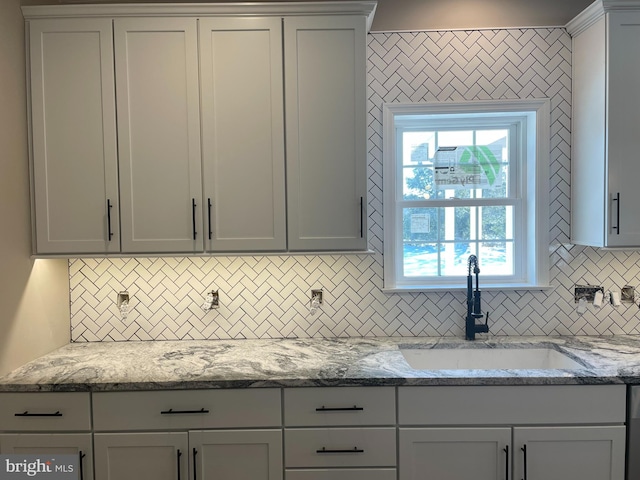 kitchen with tasteful backsplash, plenty of natural light, sink, and light stone countertops