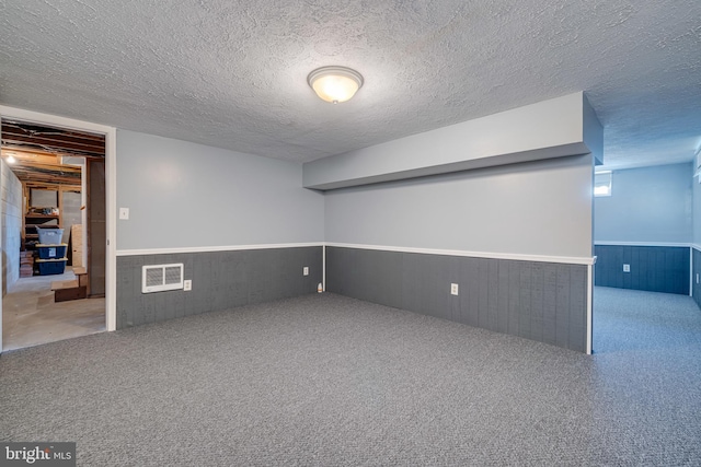 basement with visible vents, a textured ceiling, wooden walls, carpet flooring, and wainscoting