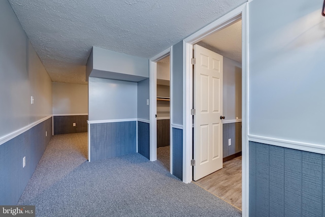 hallway with a wainscoted wall, carpet floors, a textured ceiling, and wooden walls