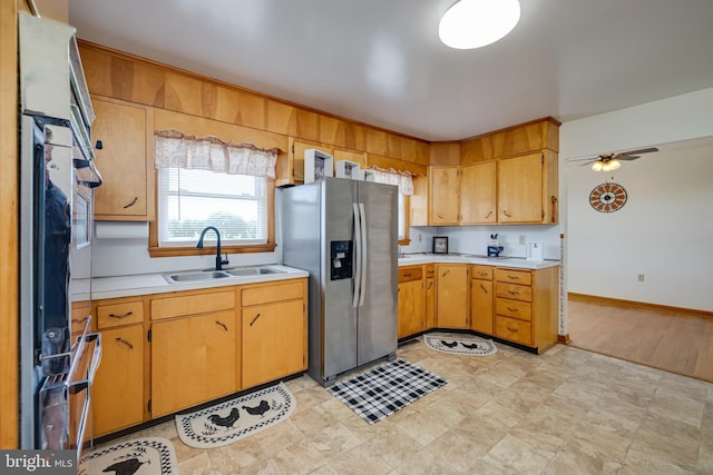 kitchen with a ceiling fan, a sink, stainless steel fridge, light countertops, and baseboards