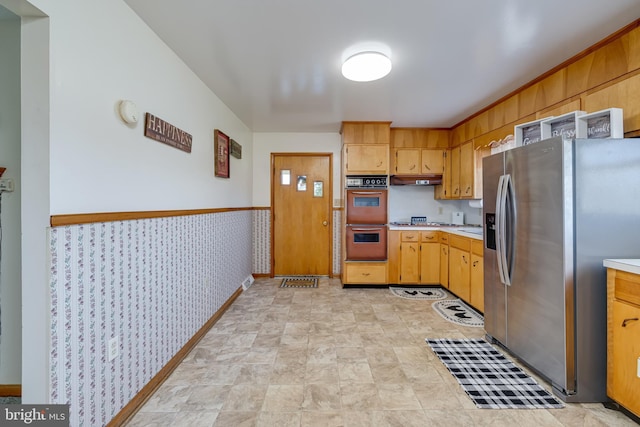 kitchen featuring stainless steel refrigerator with ice dispenser, double oven, wallpapered walls, baseboards, and light countertops