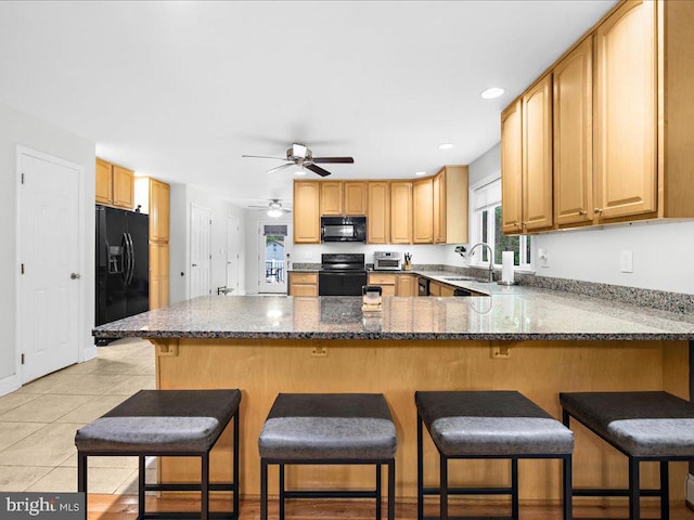 kitchen with light tile patterned flooring, a breakfast bar area, and black appliances