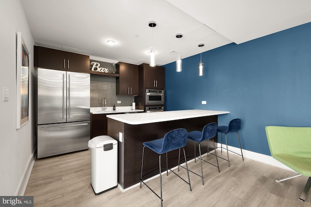 kitchen with dark brown cabinetry, decorative light fixtures, appliances with stainless steel finishes, and light hardwood / wood-style floors