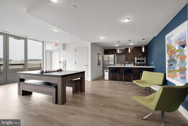 interior space with decorative light fixtures, oven, a kitchen bar, decorative backsplash, and light wood-type flooring