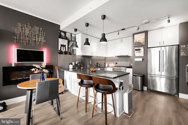 kitchen featuring appliances with stainless steel finishes, wood-type flooring, white cabinets, and hanging light fixtures