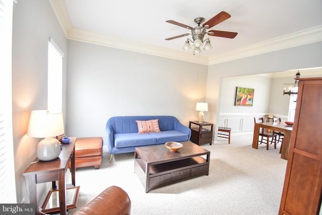 carpeted living area with crown molding and ceiling fan with notable chandelier