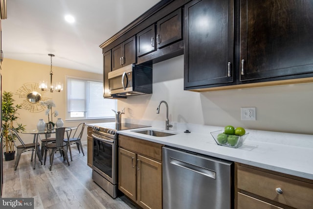 kitchen with dark brown cabinets, light wood-type flooring, sink, a notable chandelier, and stainless steel appliances