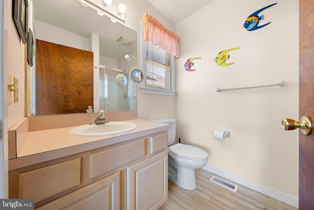 bathroom featuring hardwood / wood-style flooring, a shower with door, vanity, and toilet