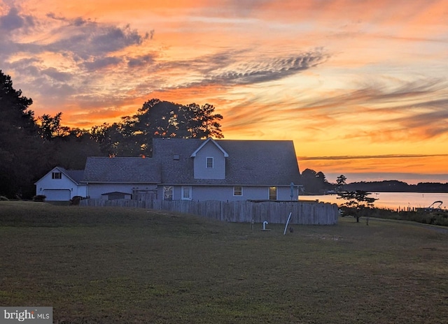 back house at dusk with a lawn and a water view