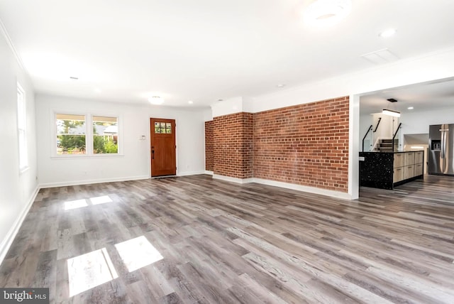 unfurnished living room featuring light hardwood / wood-style floors, brick wall, and crown molding