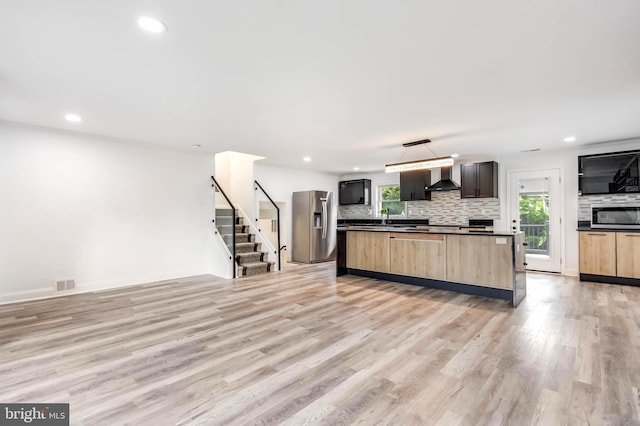 kitchen with light wood-type flooring, wall chimney range hood, decorative backsplash, appliances with stainless steel finishes, and light brown cabinetry