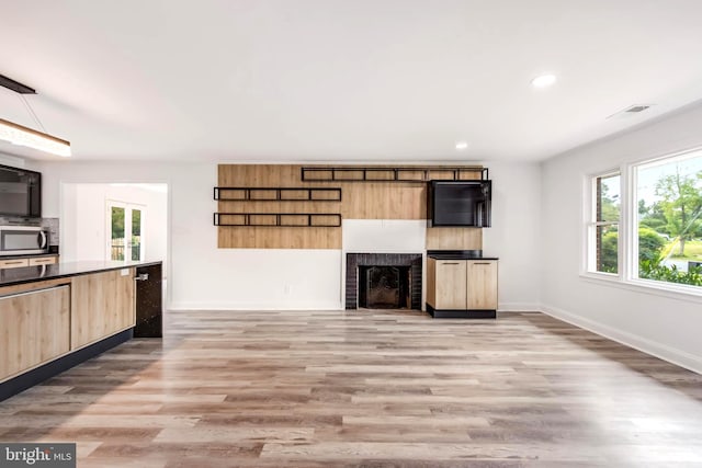 unfurnished living room featuring a healthy amount of sunlight, light hardwood / wood-style floors, and a brick fireplace