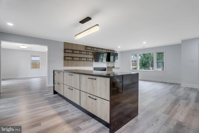 kitchen featuring dark stone counters, light hardwood / wood-style floors, light brown cabinetry, and hanging light fixtures